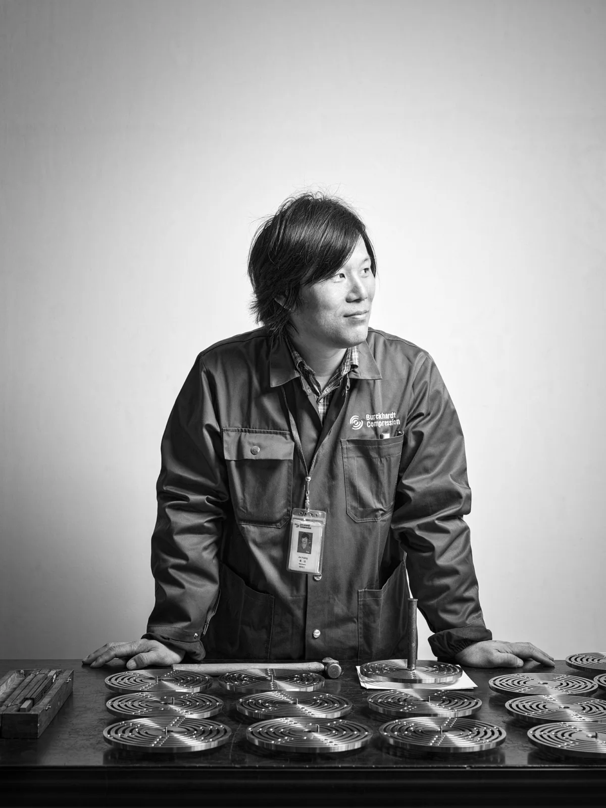 Black-and-white portrait of a Burckhardt Compression worker at a bench with compressor components, Ningbo, China, industrial photography by Scanderbeg Sauer