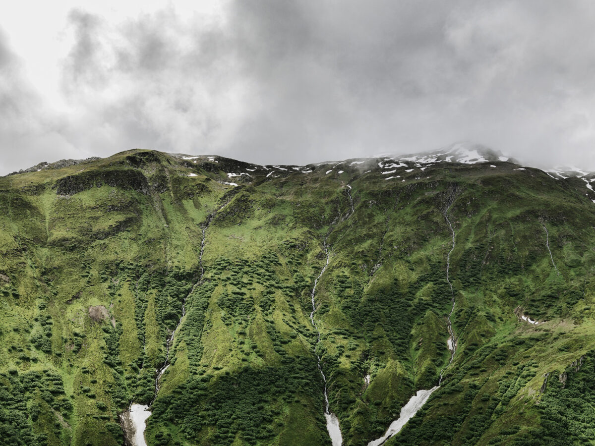 Green mountain slope with streams under clouds, Furka Pass, Obergoms, Switzerland, landscape photography by Scanderbeg Sauer