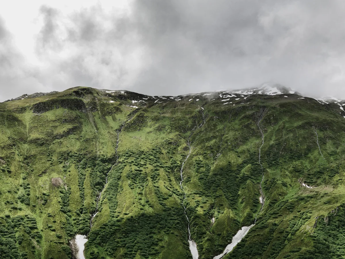 Green mountain slope with streams under clouds, Furka Pass, Obergoms, Switzerland, landscape photography by Scanderbeg Sauer