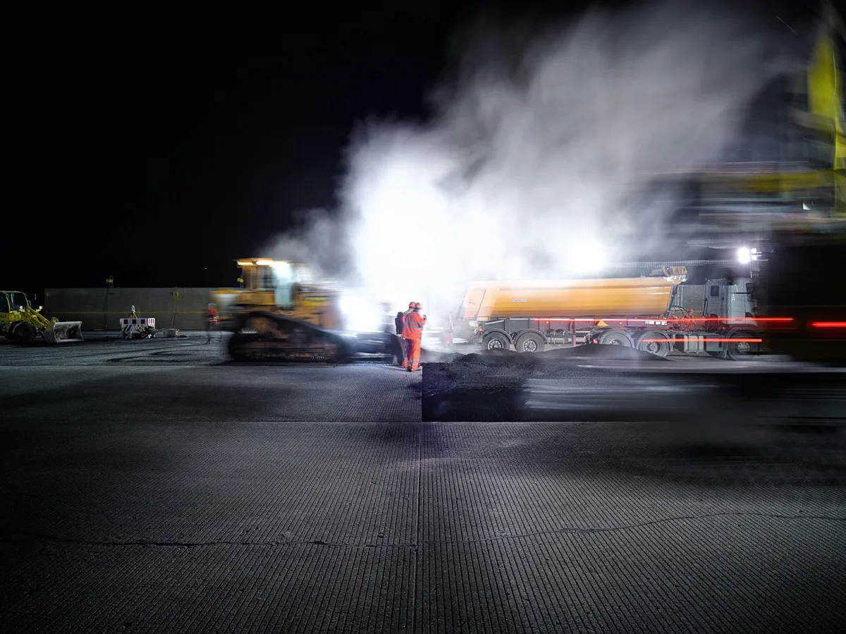 Worker on the runway at night amid steam from asphalt resurfacing at Zurich Airport, engineering photography by Scanderbeg Sauer