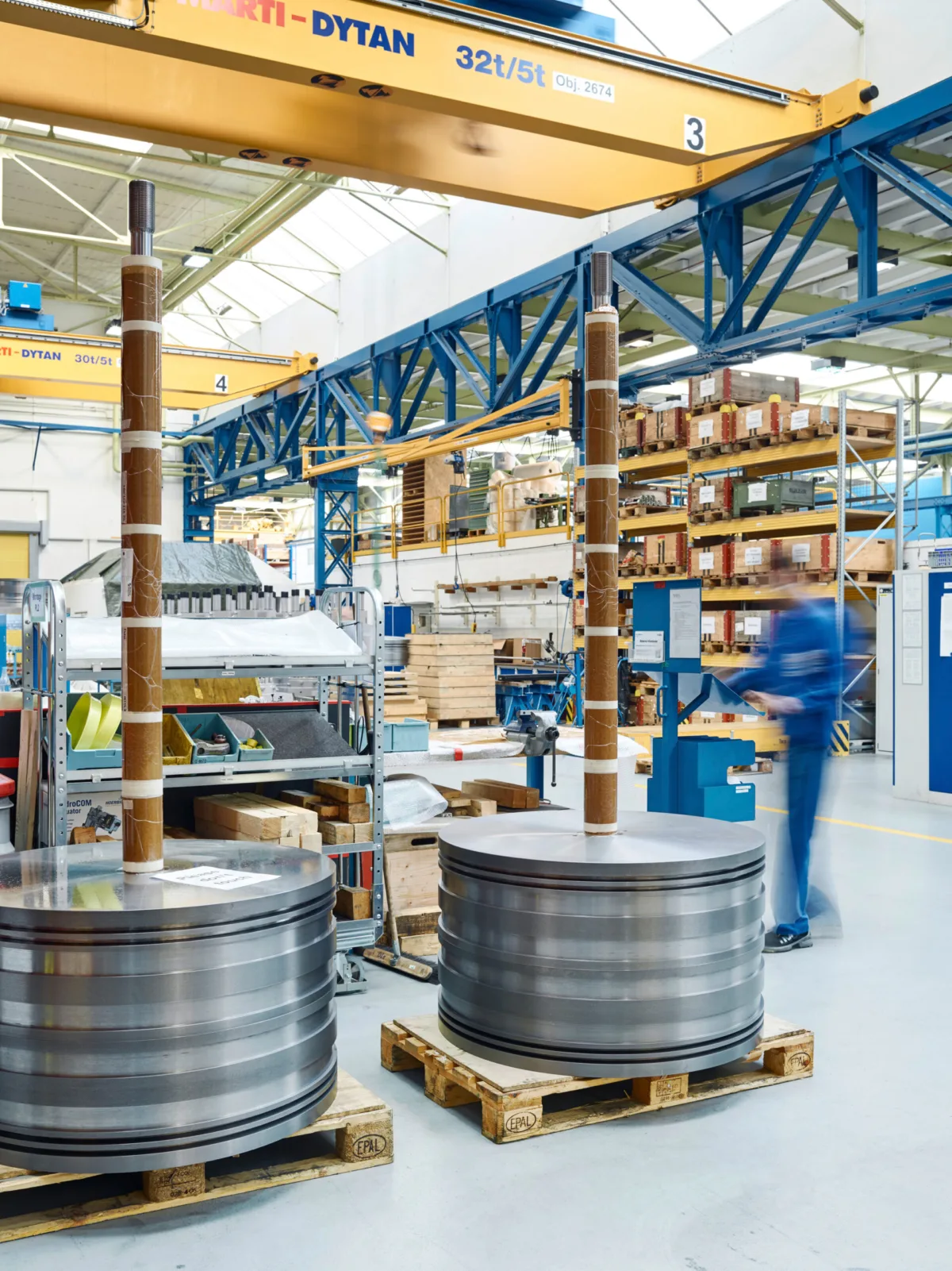 Large machined compressor components on pallets in the production hall, overhead crane above, Burckhardt Compression, Winterthur, industrial photography by Scanderbeg Sauer