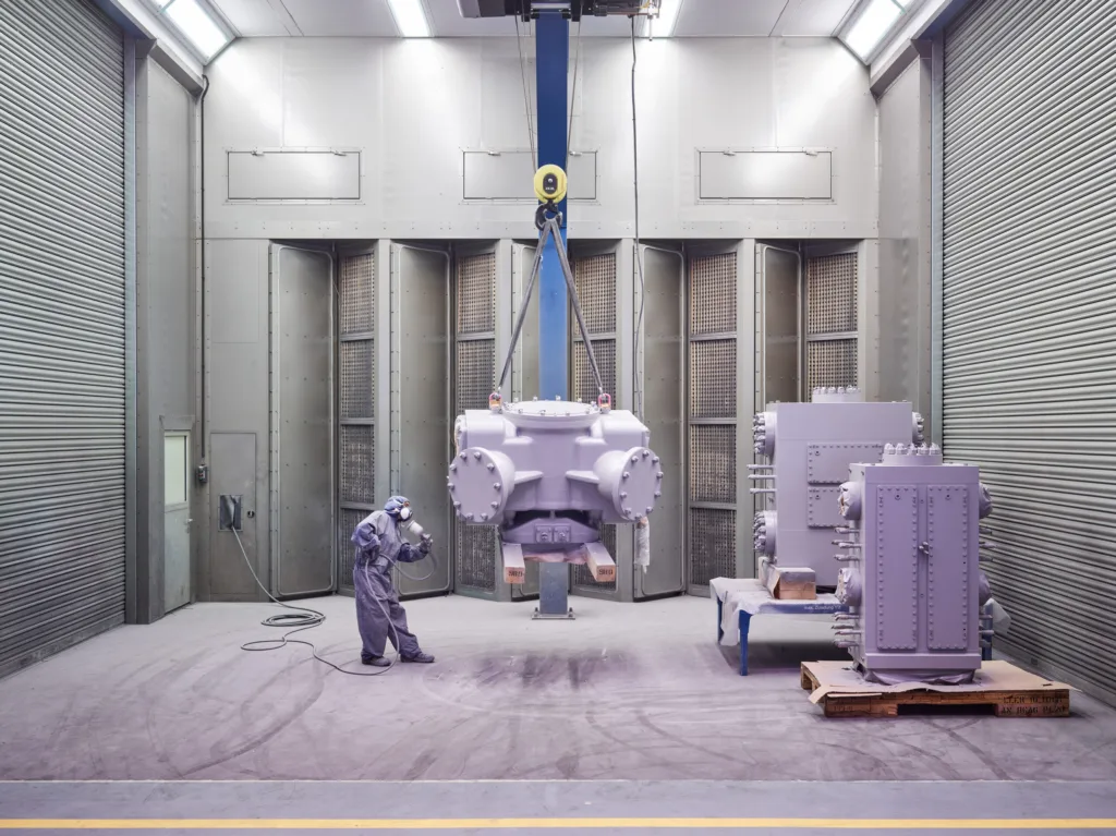 Large reciprocating compressor lifted by crane in the assembly bay, worker for scale, Burckhardt Compression, Winterthur, industrial photography by Scanderbeg Sauer