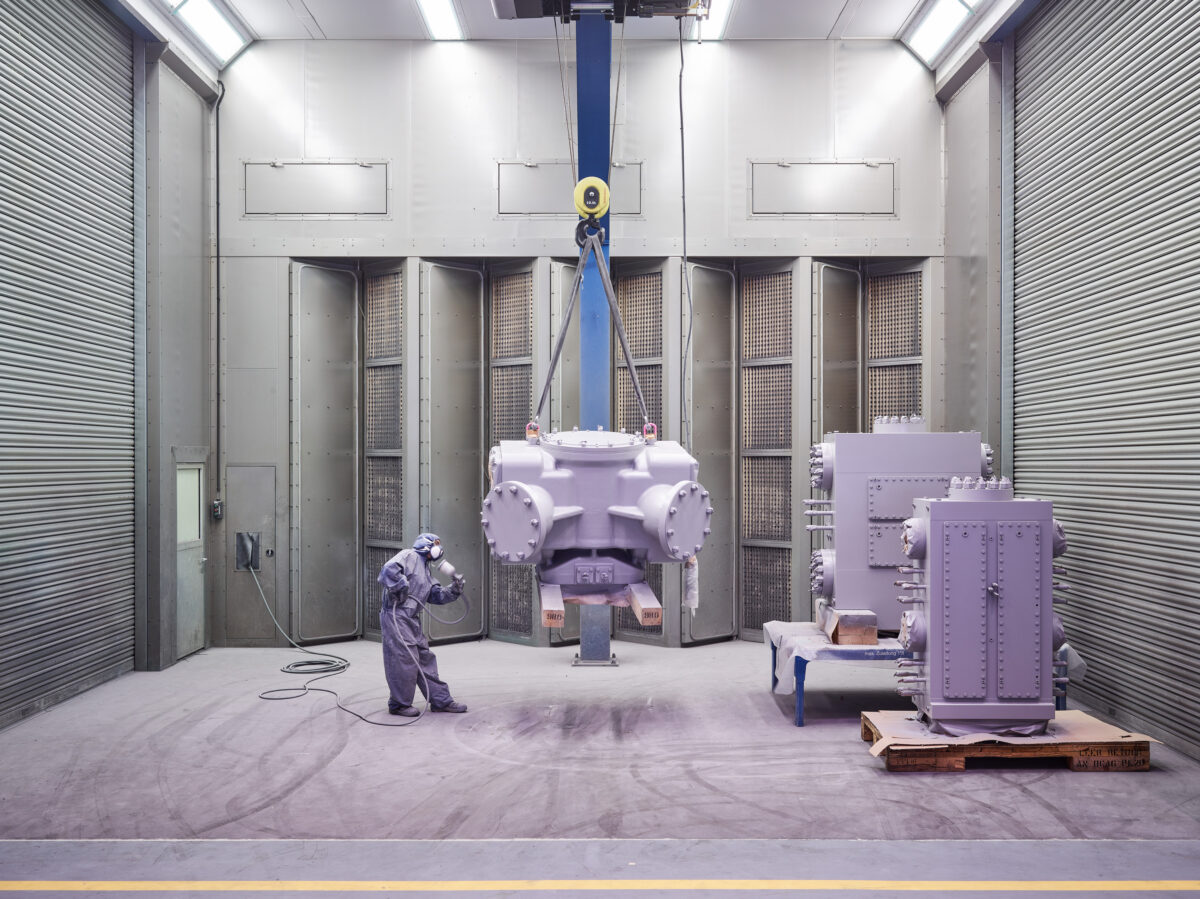 Large reciprocating compressor lifted by crane in the assembly bay, worker for scale, Burckhardt Compression, Winterthur, industrial photography by Scanderbeg Sauer