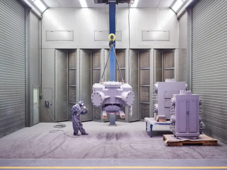 Large reciprocating compressor lifted by crane in the assembly bay, worker for scale, Burckhardt Compression, Winterthur, industrial photography by Scanderbeg Sauer