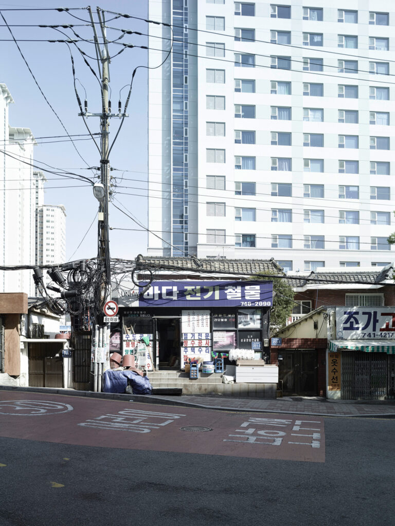 Old shops beneath a residential high-rise, Busan, South Korea, street photography by Scanderbeg Sauer
