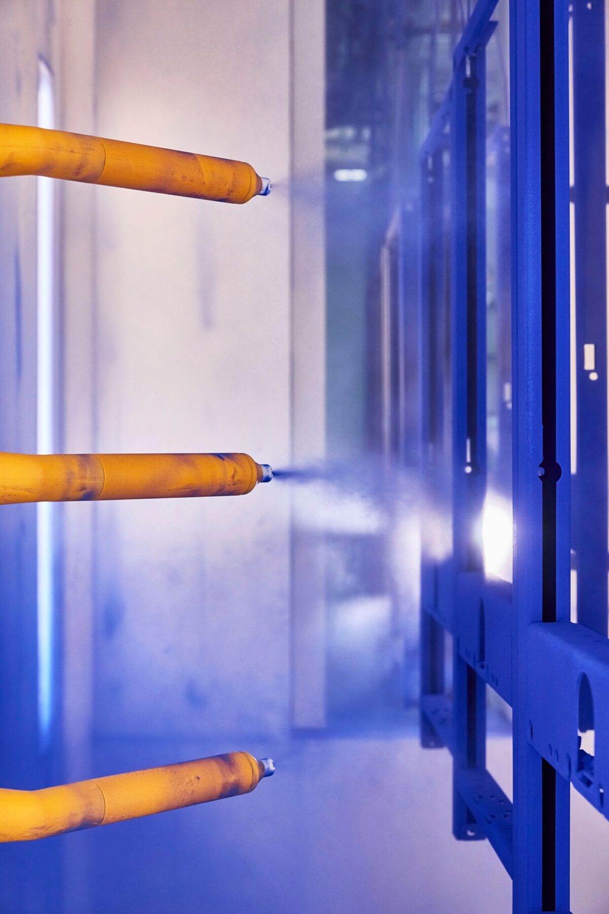 Spray guns applying coating to blue frame, Geberit production, Lichtenstein, industrial photography by Scanderbeg Sauer
