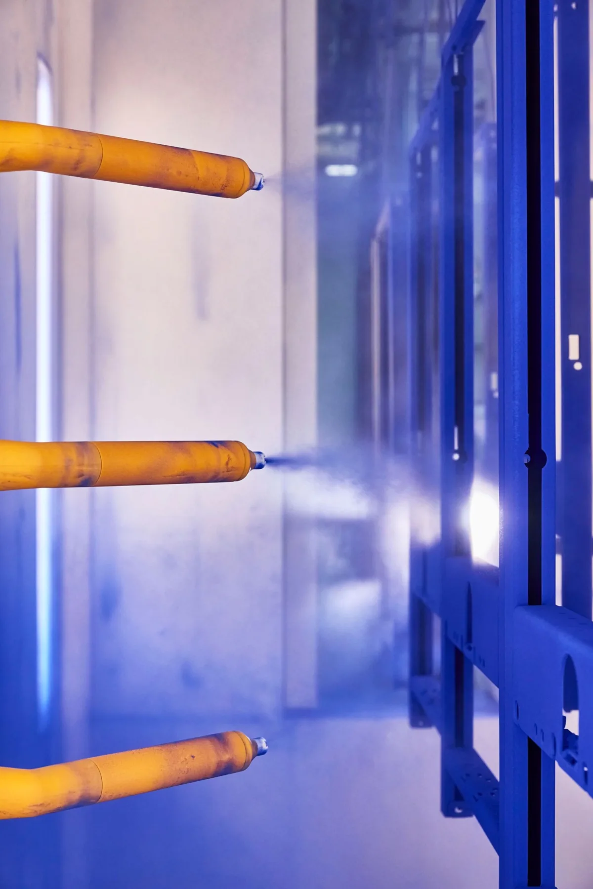 Spray guns applying coating to blue frame, Geberit production, Lichtenstein, industrial photography by Scanderbeg Sauer